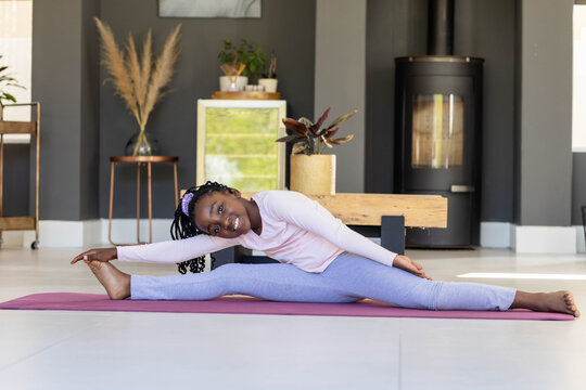 African female child stretching into side split on pink yoga mat in living room wearing leggings