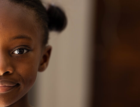 African female child showing left face with hair bun, smiling in room, wooden panel, copy space