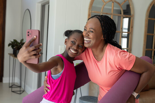 African American mother and teenage daughter taking selfie in entry holding pink phone  and  purple 
