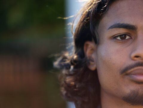 Man facing camera showing right-face closeup and wavy hair in backyard, copy space