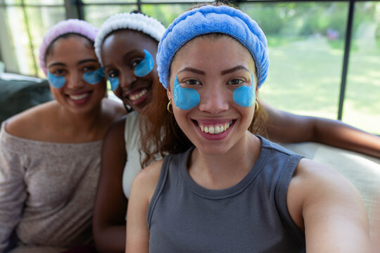 African American female friends sitting on sofa in living room, wearing headbands undereye patches