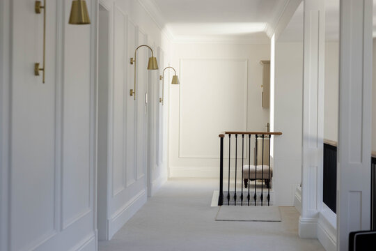 Upper-level hallway is showing staircase opening with black balusters, handrail, brass sconces