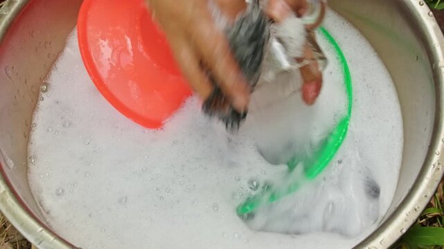 Hands washing glass and plastic plates in a stainless steel basin full of soapy foam