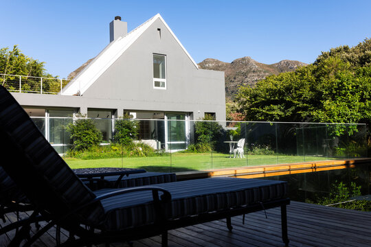 Modern gray gabled house is facing deck with striped lounge chairs and reflecting pool in backyard