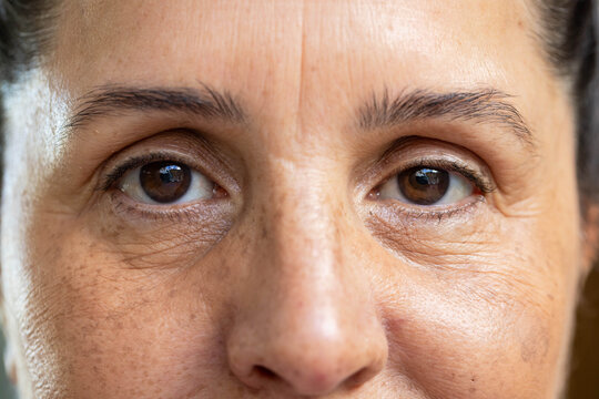 Mature woman gazing in studio near window, showing freckles, pores and bright catchlights on eyes