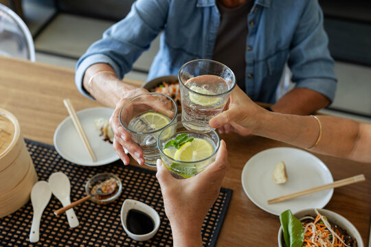 Three clear glasses are clinking on wooden table at casual dining area, with lemon and dumpling