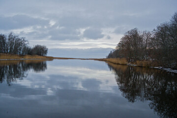 J&auml;gala river close to it`s mouth in the gulf of Finland, with bare trees m reed and clouds reflecting in the water 