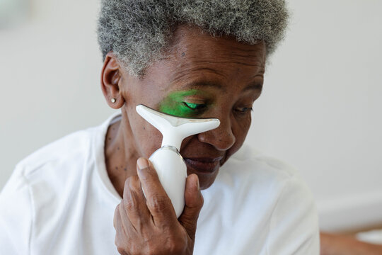Senior African American woman using white T-shaped device emitting green LED under left eye at home