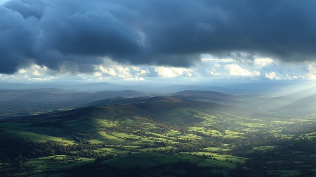 A vast, green landscape with rolling hills and distant mountains under a dramatic, cloudy sky, with sunlight filtering through the clouds and casting a warm glow over the landscape.