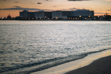 Fototapeta premium Beach coastline at dusk with distant city buildings