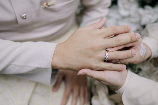 Close-up of a silver ring with a central gemstone being placed on a finger amid white floral decorations, capturing an intimate engagement moment.