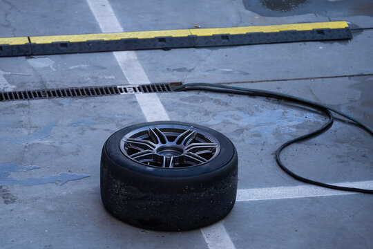 Mechanic performs automotive maintenance on red race car wheel and tire. focused pit stop service requiring precision for high speed vehicle performance and competition
