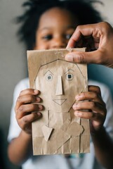 African American child holding handmade paper bag mask with drawing