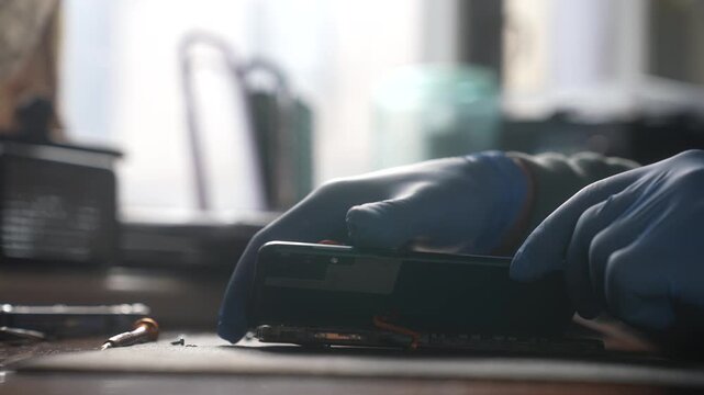 Close up of a technician hands in gloves carefully working on smartphone microchips with precision tools, highlighting the intricate process of electronic repair. Slow motion.