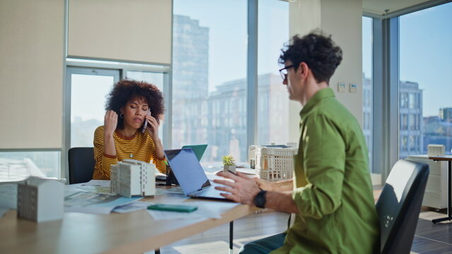 Woman realtor calling mobile phone sitting real estate agency with man colleague