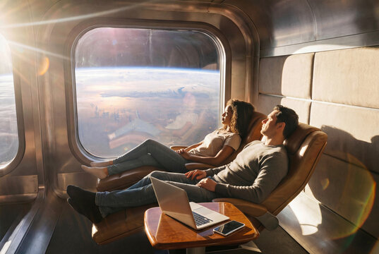 Man and woman traveling in space during futuristic space tourism tour. Couple relaxing in luxury spaceship cabin, looking at Earth through window. Space flight and interstellar travel concept.