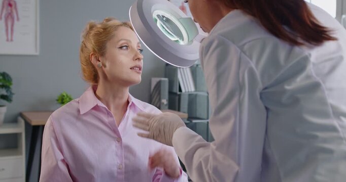 Medicine, health care and dermatology concept. Experienced dermatologist examining face of woman patient under lamp, determines condition of skin , talking about plastic surgery operation