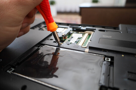 ​A technician uses an orange screwdriver to disassemble the inner case of a laptop during maintenance or repair. A detailed view of the unscrewing process reveals access to internal components like me