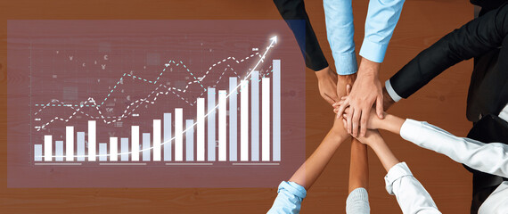 A diverse group of business professionals collaborates with hands placed together, symbolizing...