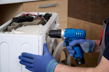 Close-up of a home appliance repair technician disassembling a washing machine with a power screwdriver.