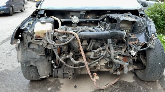 The car was seriously damaged as a result of a recent collision and a traffic accident. Close-up of car engine shows a extensive damage to the front as a result of a serious accident.