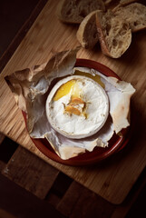 Baked Gourmet Camembert Cheese with Roasted Garlic and Melted Center on Rustic Wooden Board....
