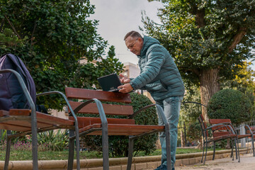 Fototapeta premium Man in park bench with laptop in autumn. Remote work, online meeting, freelance or digital business concept. Active lifestyle outside office.