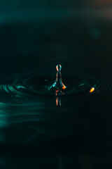 A stunning macro shot of a water drop falling into a liquid surface, creating elegant ripples. High contrast teal and orange colors on a black background. Ideal for creative design and wallpapers.
