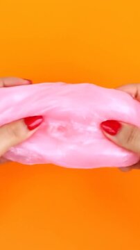 Hands with red nails playing with pink slime on orange background
