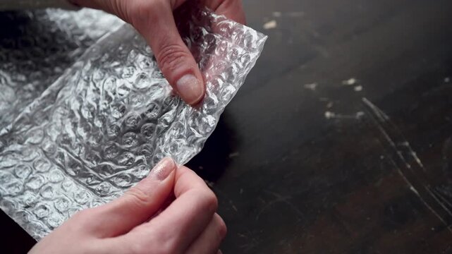 Hands popping bubbles of plastic wrap with crisp snapping sound, ASMR close-up