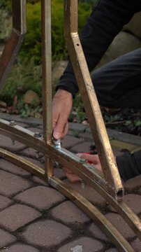 The craftsman assembles a golden wedding arch and tightens the bolts and nuts.