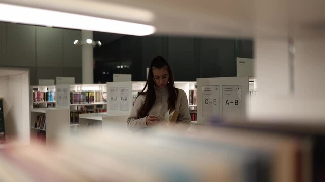 Lifestyle shot through library shelves woman in glasses reading book personal growth concept quiet moment of self education and mindfulness