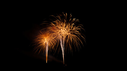 Fototapeta premium Vibrant fireworks exploding in the night sky with bright orange sparks and streaks of light against a dark background