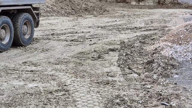 Close-up of a heavy truck reversing on a muddy construction site, tires gripping and spinning in the dirt with soil piles in the background.