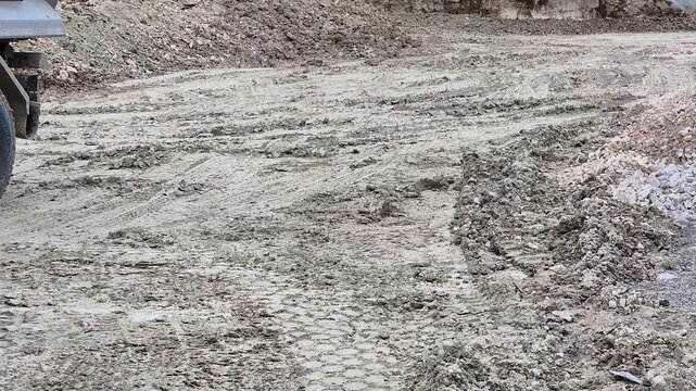 Slow motion close-up of heavy truck wheels reversing through deep mud, tires struggling for grip on a messy construction site.