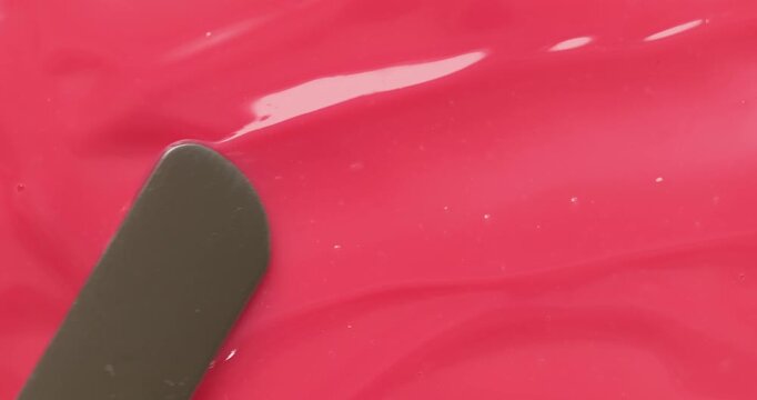Liquid pink lip gloss cosmetic texture close up with metal spatula tool. Beauty make up abstract