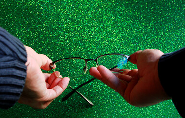 Gafas graduadas de ver en manos de persona con fondo verde brillo