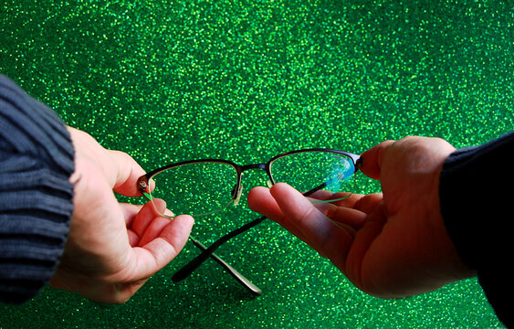 Gafas graduadas de ver en manos de persona con fondo verde brillo
