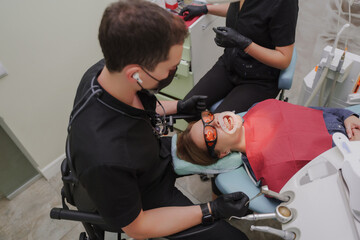 The dentist treats the patient. Patient with dilator in mouth and wearing goggles sitting in chair at dentist's appointment. Dentist, nurse and patient. The process of dental treatment.