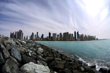 Wide panoramic view of Dubai Marina skyline across calm waterfront, modern skyscrapers reflecting daylight, showcasing architecture, coastal cityscape, travel destination.