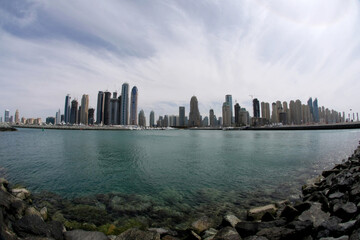 Wide panoramic view of Dubai Marina skyline across calm waterfront, modern skyscrapers reflecting daylight, showcasing architecture, coastal cityscape, travel destination.