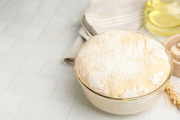 Yeast dough in bowl and ingredients on white tiled table, closeup. Space for text