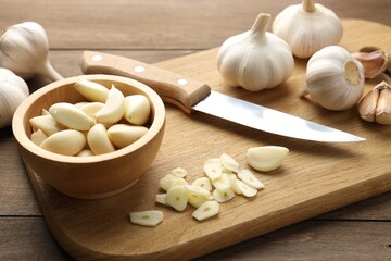 Fresh garlic bulbs, cloves and knife on wooden table, closeup