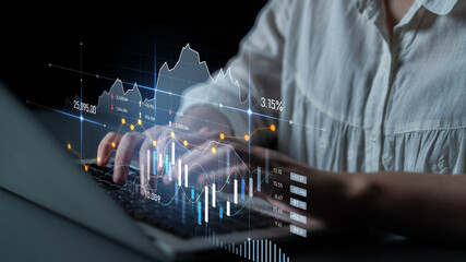 A person interacts with a laptop to analyze stock market data displayed through graphs and...