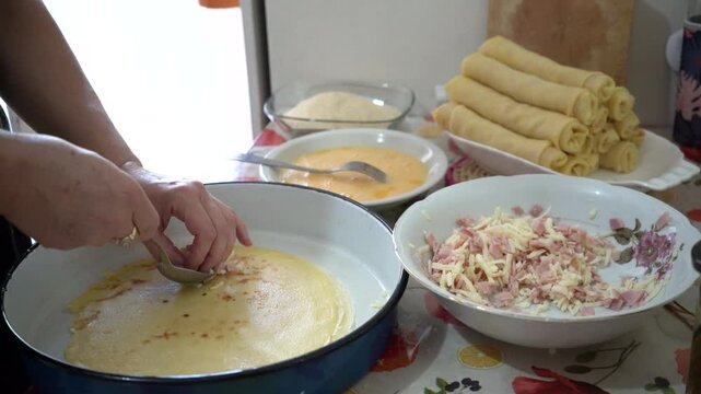 A woman fills a pancake with grated ham and cheese, then folds it neatly