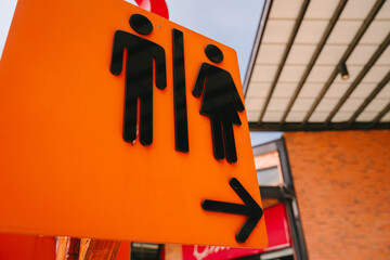 Restroom sign with male and female symbols on orange background pointing right in urban setting