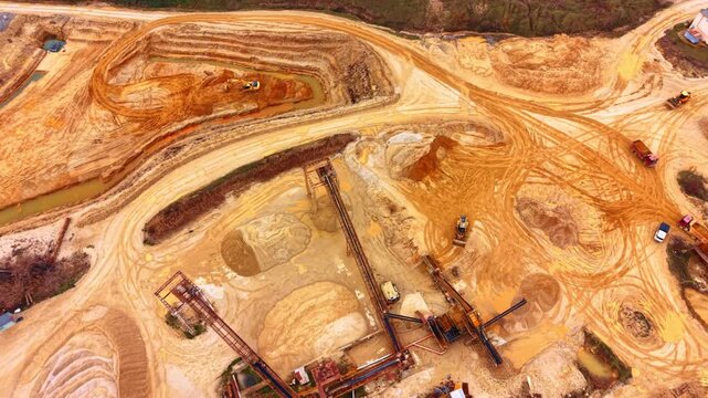 Industrial site with conveyors and heavy equipment in quarry. High angle overview of sand processing area with conveyor belts, wheel loaders, and multiple trucks.