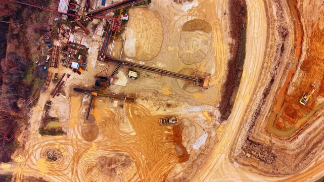 Industrial machinery and conveyor in quarry. Vertical top down shot of quarry infrastructure, conveyor belts, wheel loaders, and tire tracks on sand.