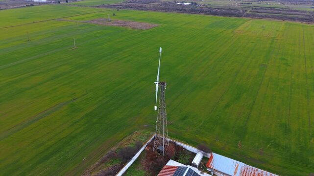 Wind turbine tower in green agricultural field aerial. A single wind generator on a lattice mast in a vast green field for renewable energy.