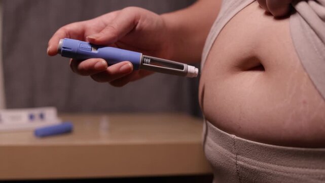 A horizontal close up of an young woman giving an injection to her belly
A young woman giving an injection of semaglutide to her belly